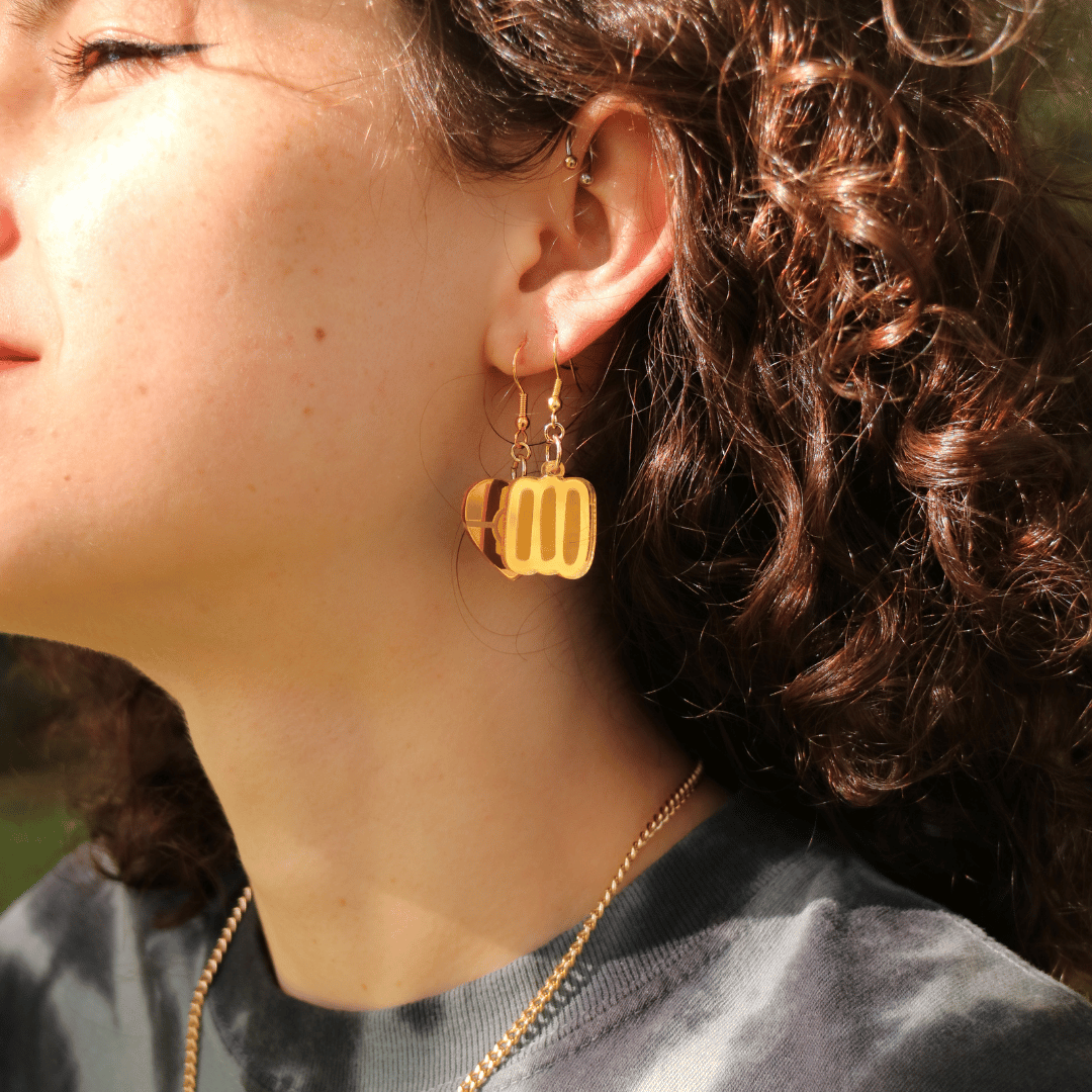 close up of model wearing haus of dizzy gold markings mirror earrings in size extra small. the earrings feature aboriginal art which that typically represents Aboriginal body paint and tribal markings