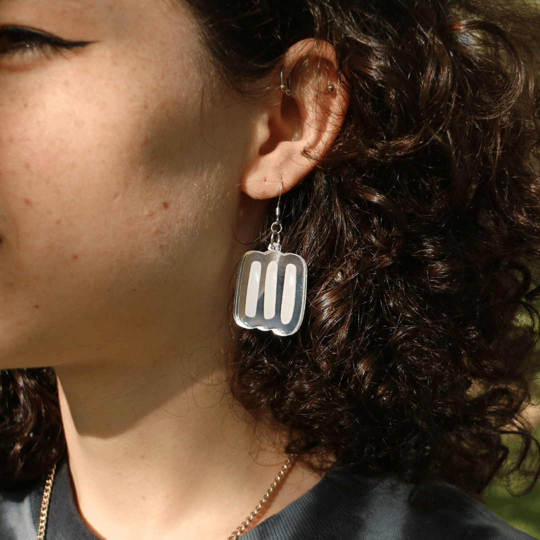 close up of model wearing haus of dizzy silver markings mirror earrings in size small. the earrings feature aboriginal art which that typically represents Aboriginal body paint and tribal markings.