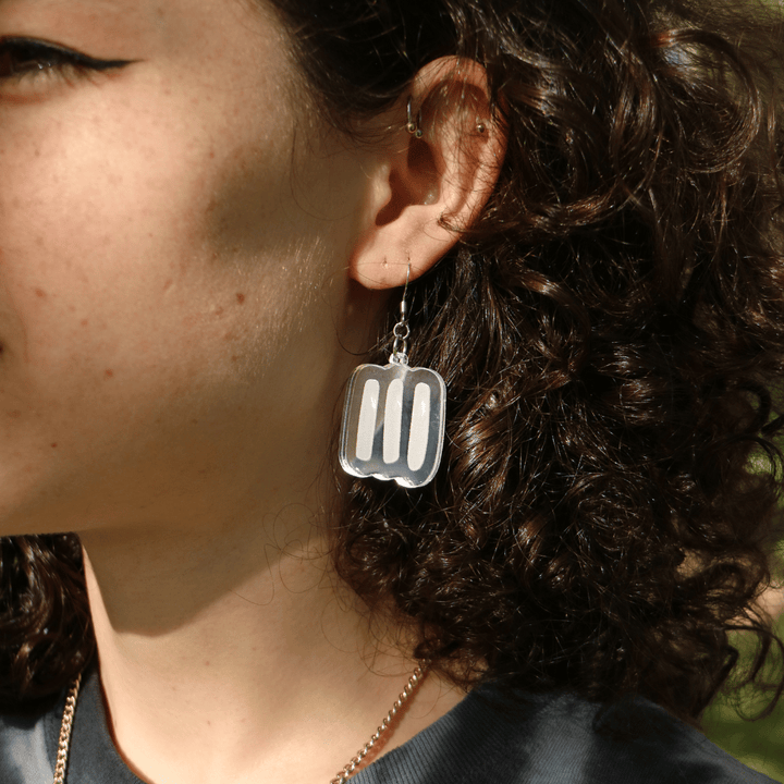 close up of model wearing haus of dizzy silver markings mirror earrings in size small. the earrings feature aboriginal art which that typically represents Aboriginal body paint and tribal markings.