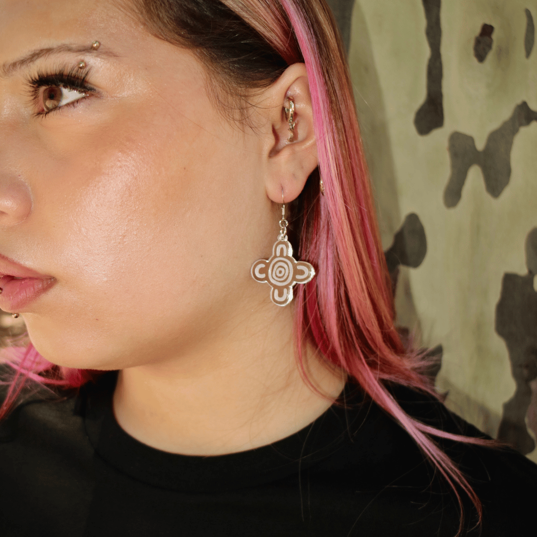 close up of model wearing haus of dizzy meeting place mirror earrings size small silver mirror with a blurred natural background. the earring features aboriginal art which represents people coming together, seated at a specific site, camp or gathering place.