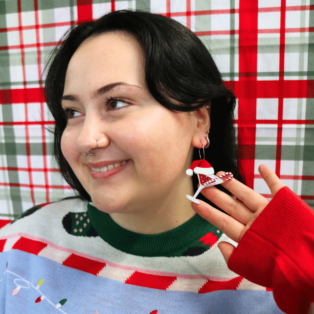 model wearing ugly christmas sweater against a red and green plaid background. she is wearing haus of dizzy merry martini earrings and looking away from camera