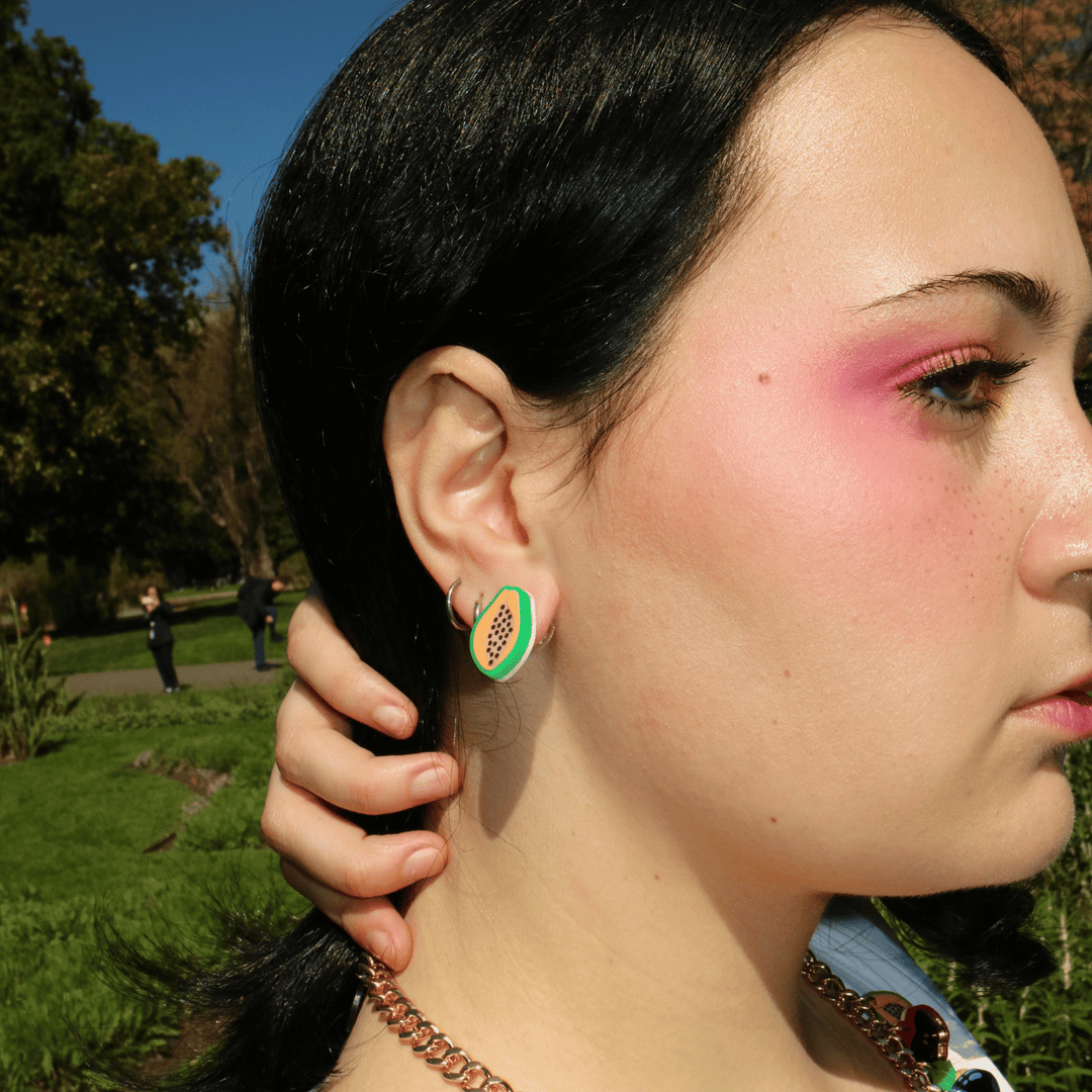 side profile shot close up of model wearing haus of dizzy's papaya studs which have green, orange, and blush acrylic with hand painted black seeds.