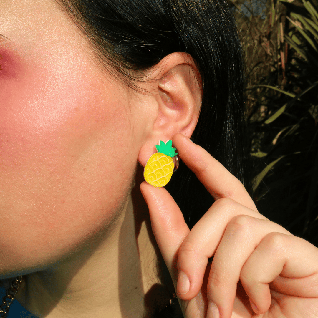 close up shot of model wearing haus of dizzy's pineapple studs which have transparent yellow acrylic and matte green acrylic.