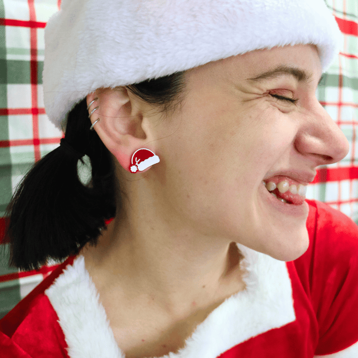 model wearing santa hat withhaus of dizzys santas swag studs in red gloss, looking away from camera making a cheeky face