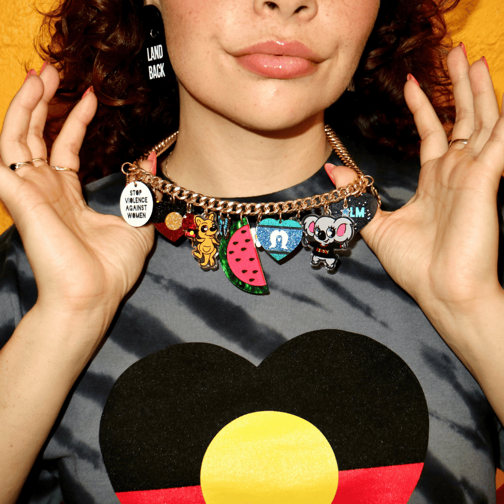 a close up image of haus of dizzy social justice necklace ona. model, with half her face cut off, focussed on the charm necklace. the necklace features multiple different charms like cartoon native australian animals,glitter heart flags and acronyms for social justice issues.