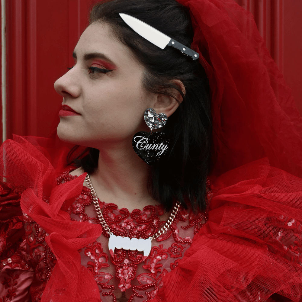 image of model in red bridal halloween costume wearing haus of dizzy stabby knives hair clips in silver mirror, as well as haus of dizzy earrings and necklace