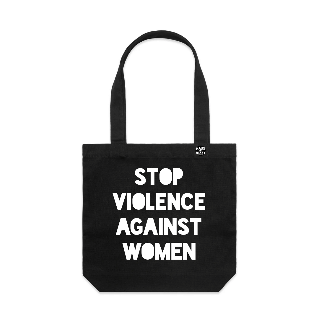haus of dizzys black canvas tote bag with two shoulder straps, featuring the printed text 'STOP VIOLENCE AGAINST WOMEN' in white bold text. A small circular logo is printed on the upper right side of the bag.