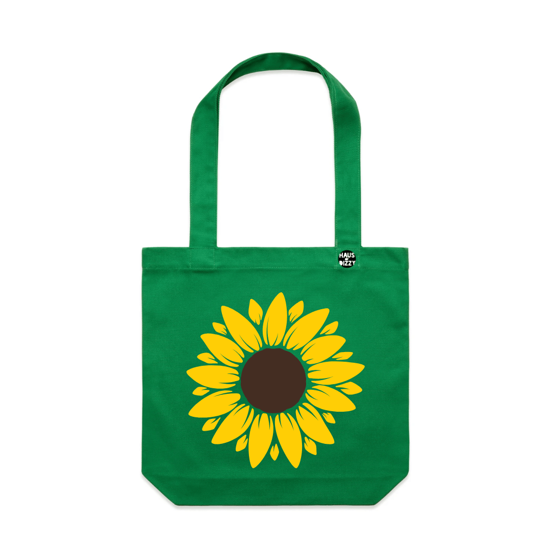 an image of Haus of Dizzy's sweet sunflower tote bag. Pictured is a green tote bag with a a large image of a sunflower in the centre with Haus of Dizzy's logo on the front strap.