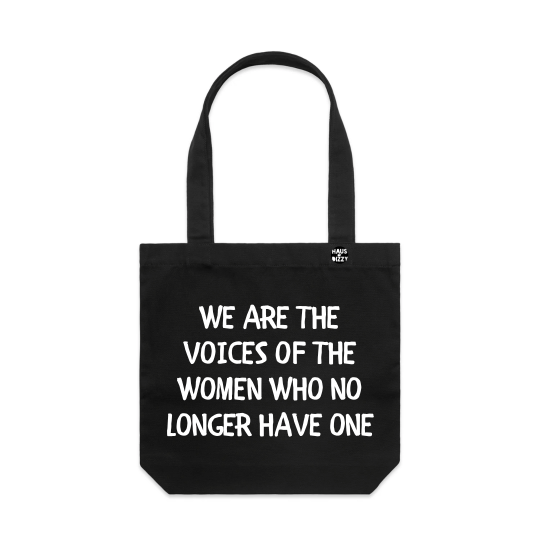 haus of dizzys black canvas tote bag with two shoulder straps, featuring the printed text 'WE ARE THE VOICES OF THE WOMEN WHO NO LONGER HAVE ONE' in bold white text. A small circular logo is printed on the upper right side of the bag.