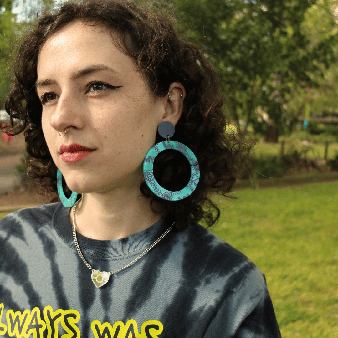 model wearing haus of dizzy wiradjrui yinaa earth tones hoop earrings in dusty teal colour, outdoors with greenery in the background