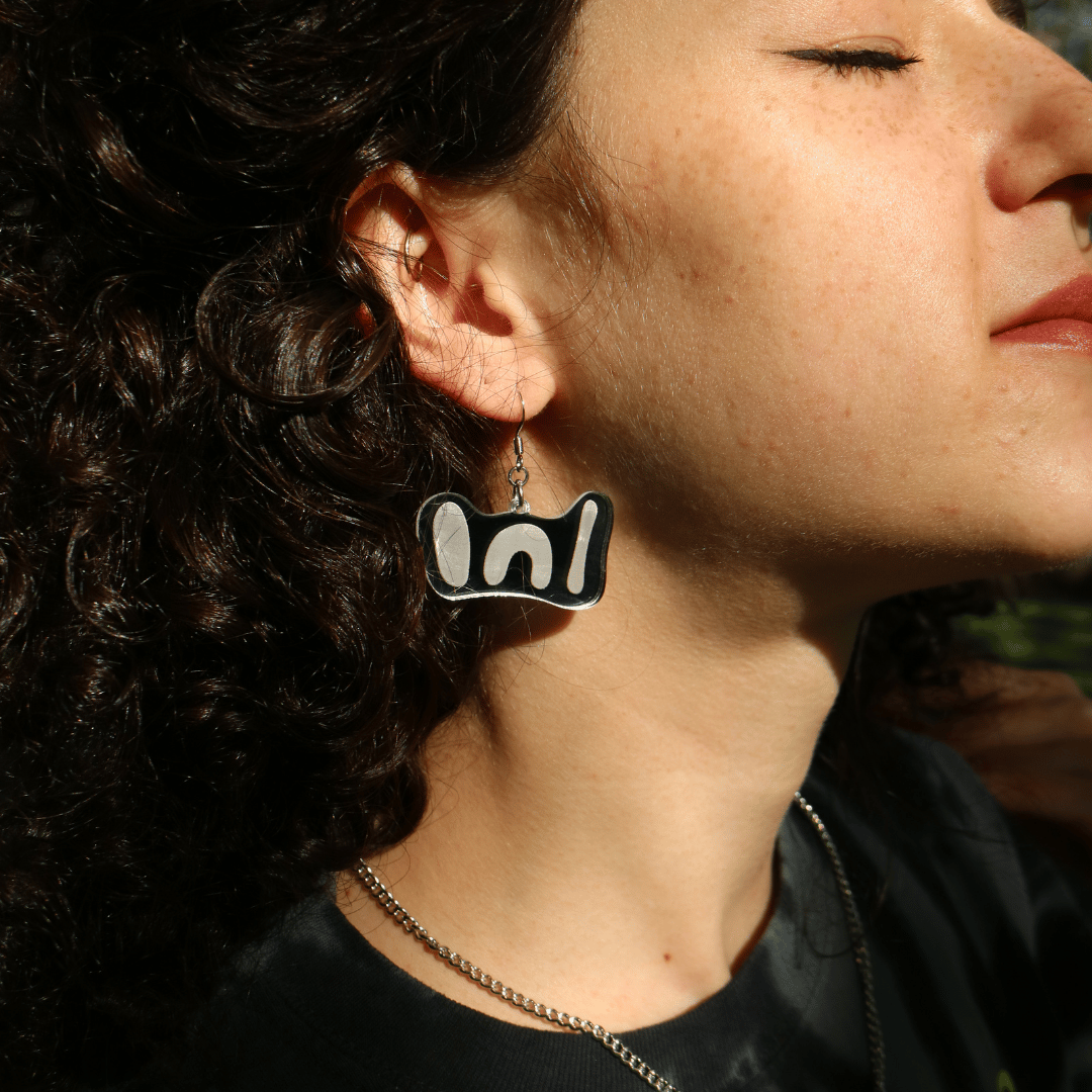 close up of model in the sun wearing haus of dizzy 'woman' mini mirror earrings in silver mirror.