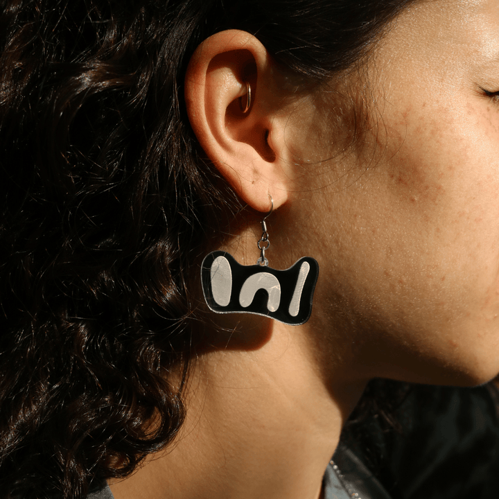 close up of model in the sun wearing haus of dizzy 'woman' mini mirror earrings in silver mirror.