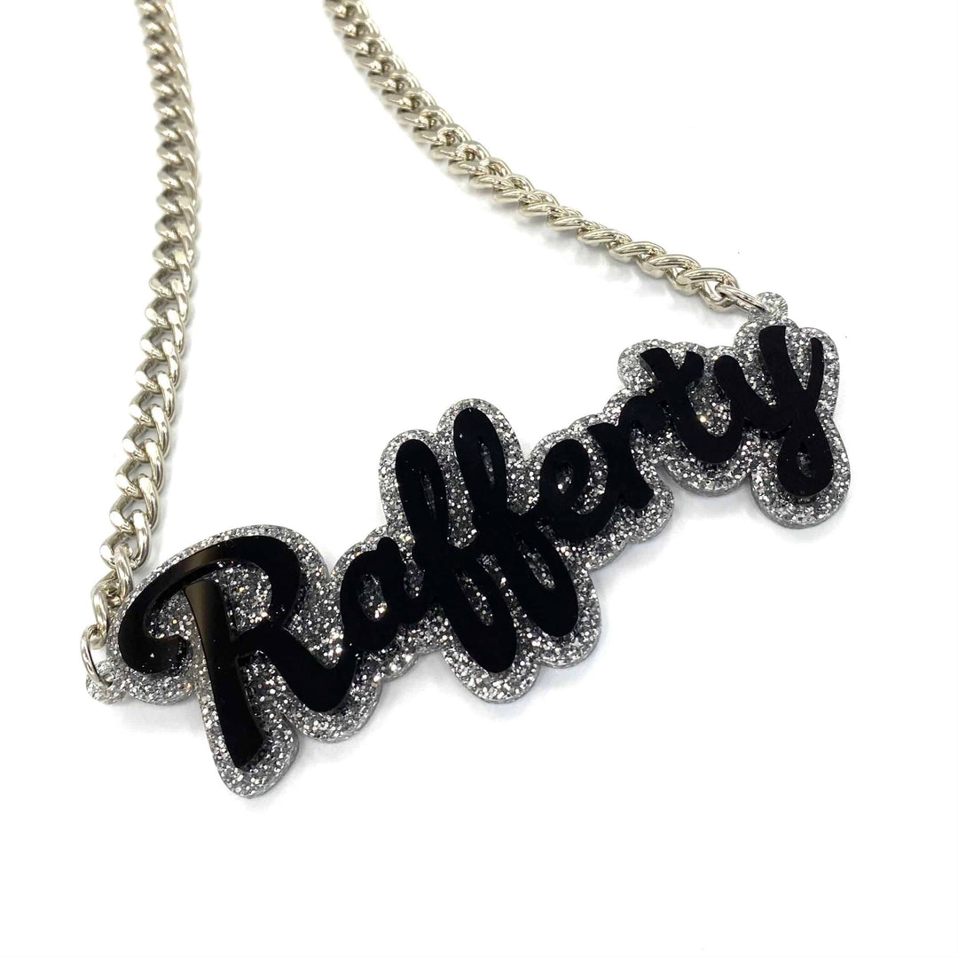 haus of dizzy custom name necklace. silver glitter background with black text that reads rafferty on silver chain