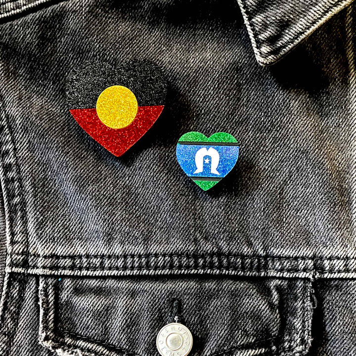close up shot of denim jacket with haus of dizzy's first nations pride heart pins the aboriginal flag is in the size large and the torres strait is size small